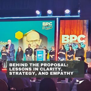 A conference stage with people standing and holding awards, a large screen displaying 'Congratulations on your retirement' with an image of a man, and an audience seated in front. Text overlay reads: 'BEHIND THE PROPOSAL: LESSONS IN CLARITY, STRATEGY, AND EMPATHY.' Logos for BPC Nashville and BPC are visible.