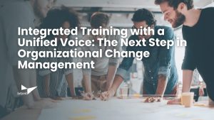 A diverse group of four colleagues stands around a table, collaborating and smiling as they review plans and notes. The text overlay reads: 'Integrated Training with a Unified Voice: The Next Step in Organizational Change Management.' The Briljent logo appears in the bottom left corner.