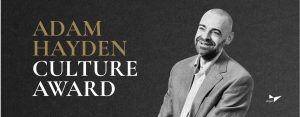 Portrait of a man in a gray suit jacket and checkered shirt beside text announcing the Adam Hayden Culture Award by Briljent.