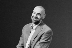 Portrait of a man in a gray suit jacket and checkered shirt.