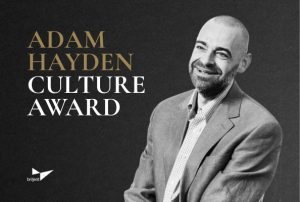 Portrait of a man in a gray suit jacket and checkered shirt beside text announcing the Adam Hayden Culture Award by Briljent.