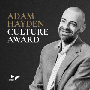 Portrait of a man in a gray suit jacket and checkered shirt beside text announcing the Adam Hayden Culture Award by Briljent.